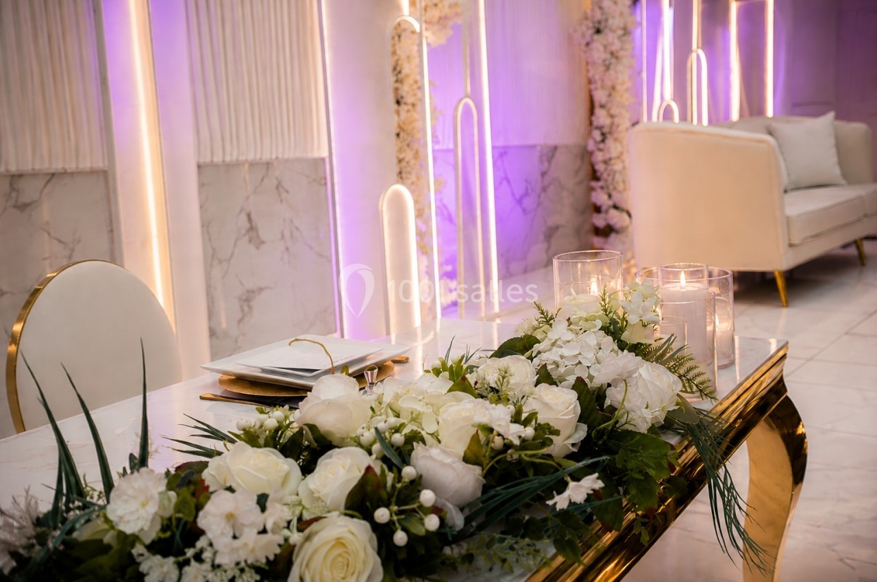 Table décorée avec des fleurs blanches et des bougies, dans une salle élégante aux tons mauves et dorés.