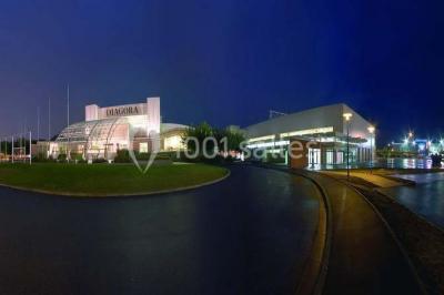 Salle circulaire avec tables rondes dressées, nappes grises et serviettes vertes, entourée de baies vitrées donnant sur des…