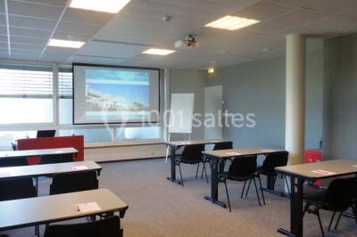 Salle circulaire avec tables rondes dressées, nappes grises et serviettes vertes, entourée de baies vitrées donnant sur des…