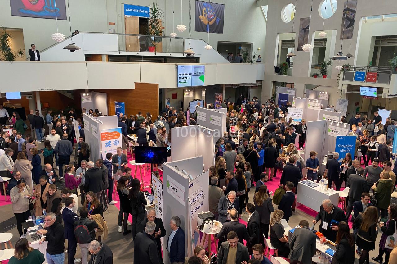 Vue d'un salon professionnel animé avec des stands, des visiteurs et une ambiance conviviale dans un espace intérieur.