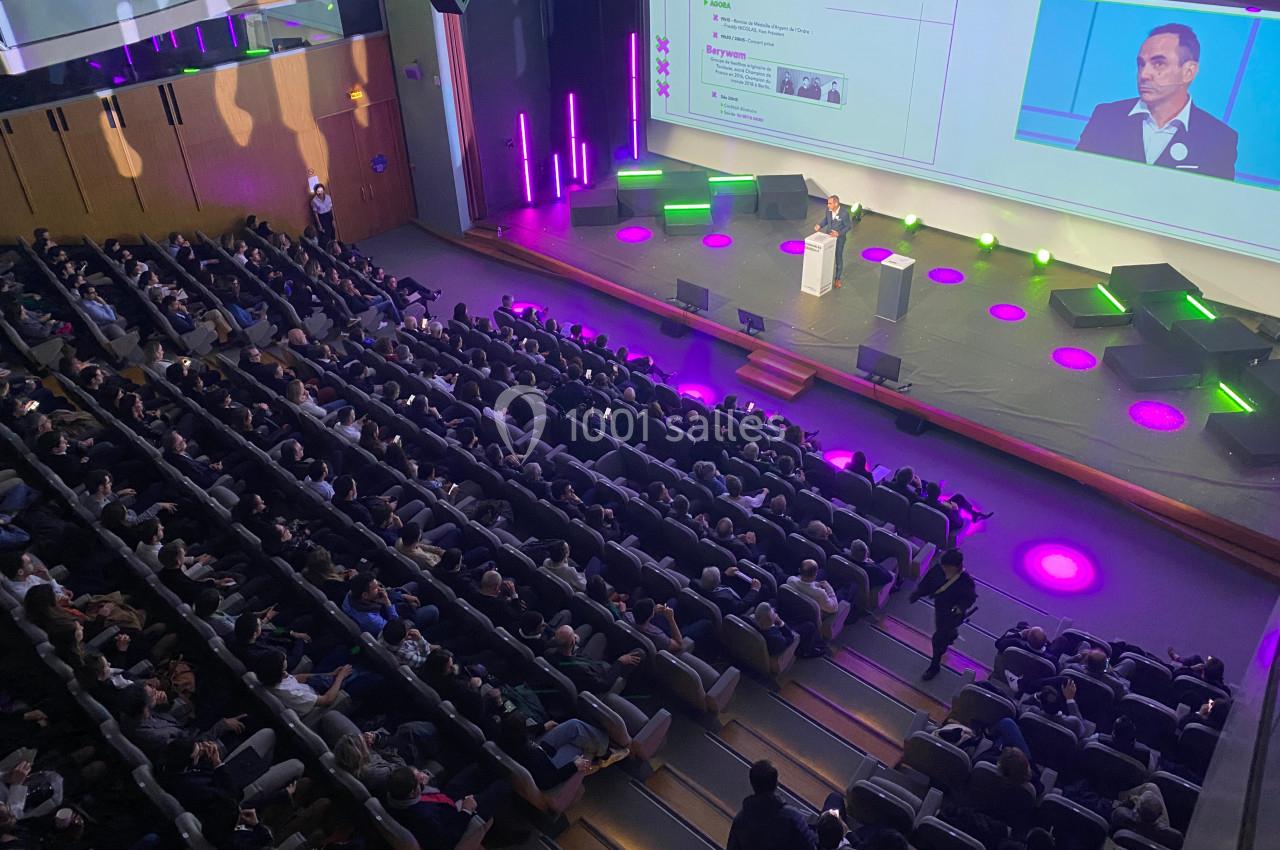 Vue d'une conférence dans un auditorium, avec un orateur sur scène et un public nombreux assis.