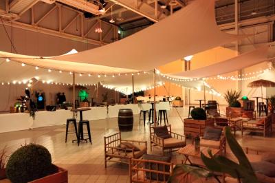 Salle circulaire avec tables rondes dressées, nappes grises et serviettes vertes, entourée de baies vitrées donnant sur des…