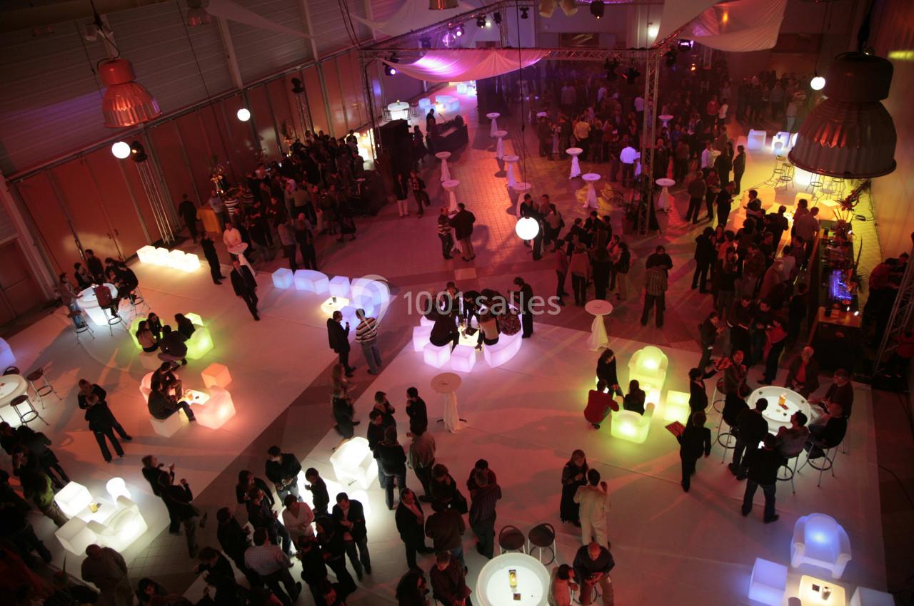 Salle événementielle animée avec des groupes de personnes autour de tables lumineuses et un éclairage tamisé.