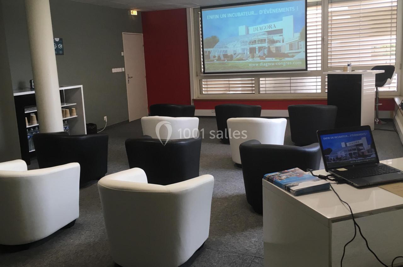 Salle de réunion avec fauteuils disposés face à un écran de projection et un ordinateur portable sur un bureau.