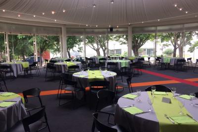Salle circulaire avec tables rondes dressées, nappes grises et serviettes vertes, entourée de baies vitrées donnant sur des…