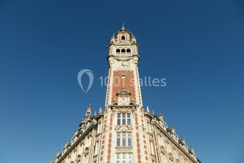 Tour d'un bâtiment historique en briques rouges avec une horloge, sous un ciel bleu clair.