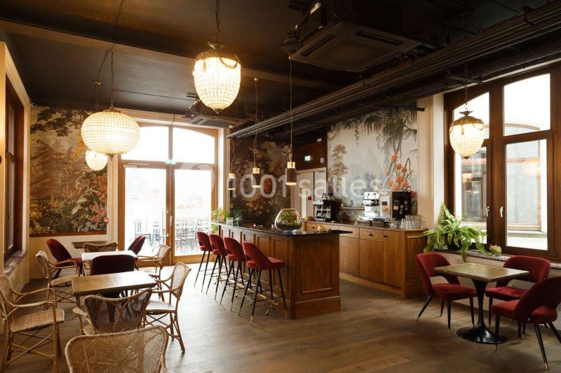Salle lumineuse avec un bar en bois, des tables et des chaises, décorée de plantes et de papiers peints à motifs naturels.