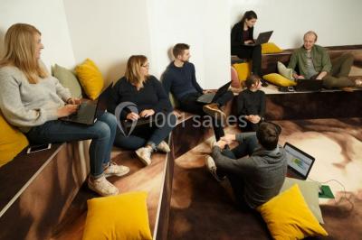 Personnes rassemblées sous une tente verte sur une terrasse, avec des plantes en pot et des clochers en arrière-plan.
