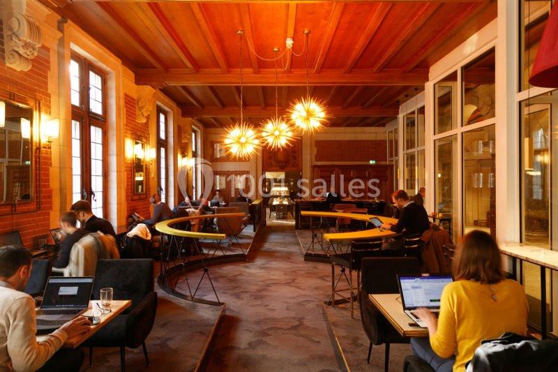 Salle lumineuse avec des plafonds en bois, des tables occupées par des personnes travaillant sur des ordinateurs.