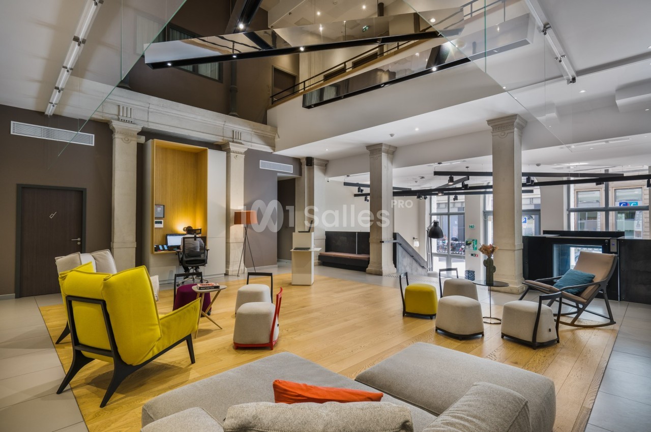 Espace de réception moderne avec fauteuils colorés, tables basses et éclairage naturel dans un décor contemporain.