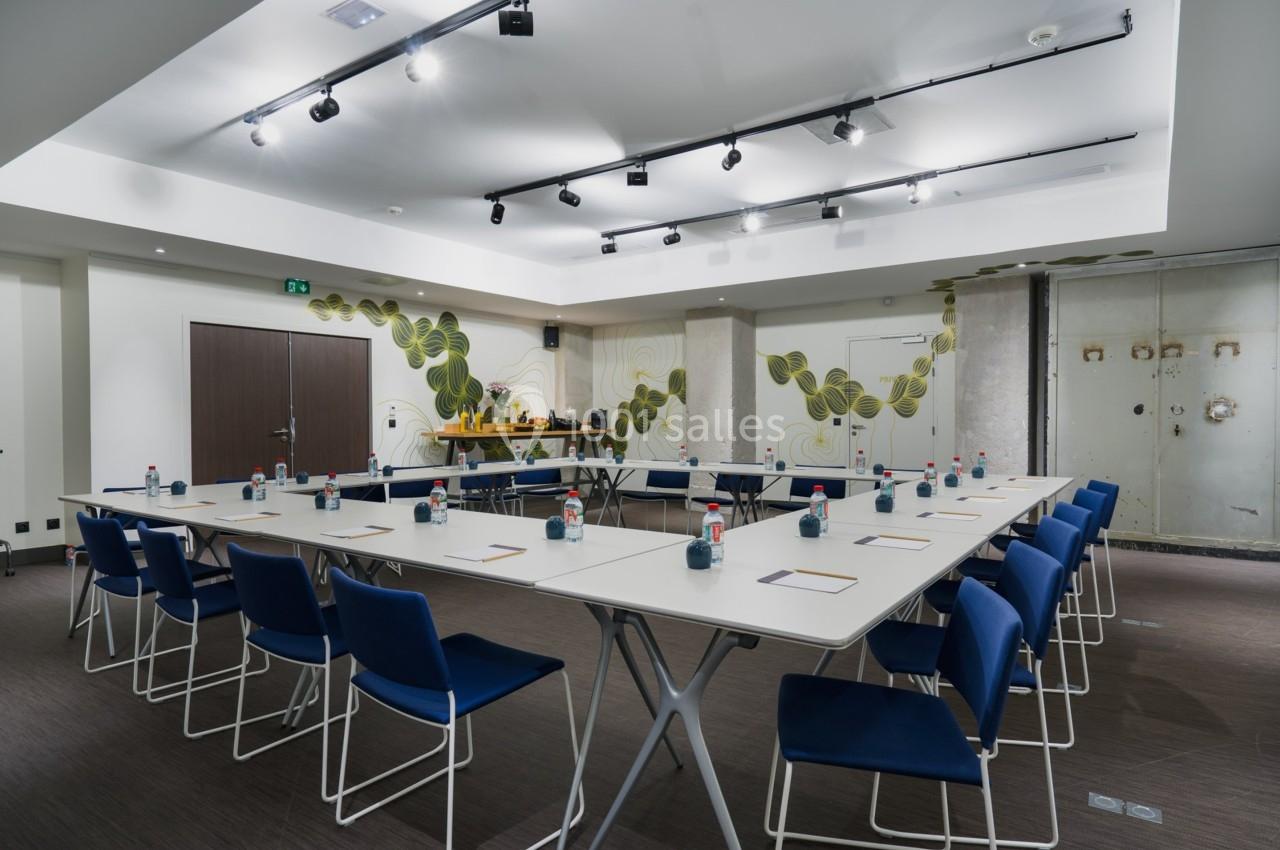 Salle de réunion moderne avec tables disposées en U, chaises bleues et décor mural végétal.