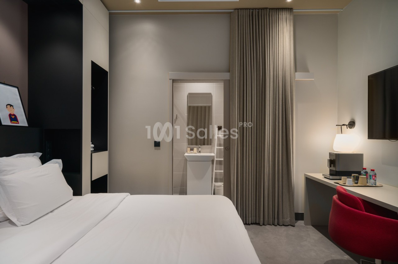 Chambre d'hôtel moderne avec lit double, bureau, télévision murale et salle de bain visible à travers une porte ouverte.