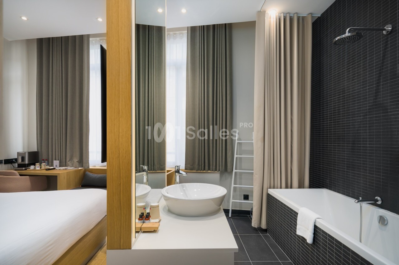 Salle de bain moderne avec lavabo, baignoire, douche à l'italienne et vue partielle sur une chambre lumineuse.