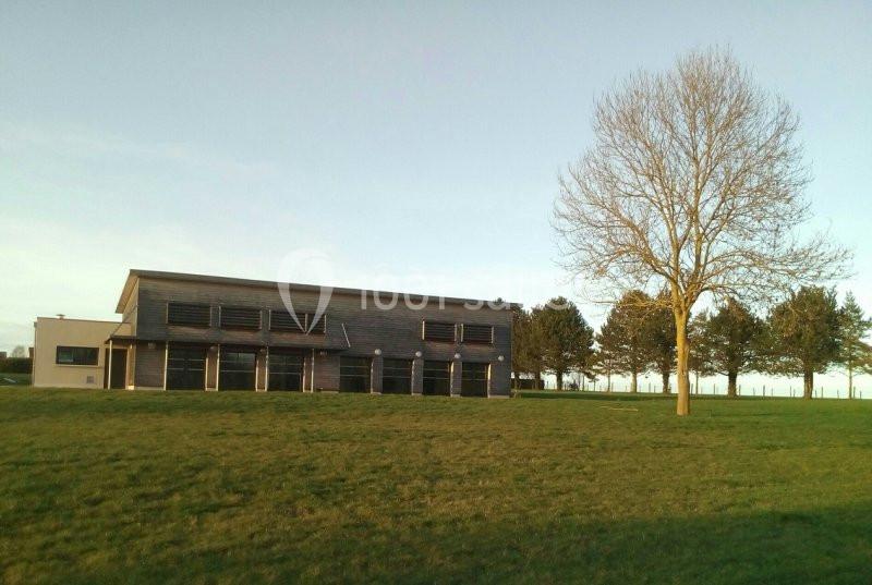 Bâtiment moderne en bois entouré d'un grand espace vert avec un arbre isolé et des arbres en arrière-plan.