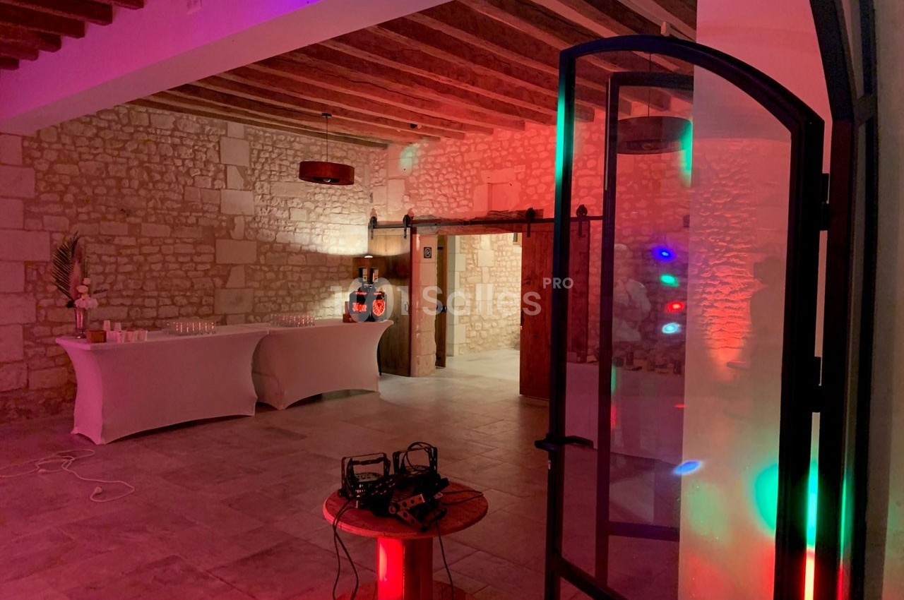 Salle en pierre éclairée par des lumières colorées, avec une table dressée et des équipements audio visibles.