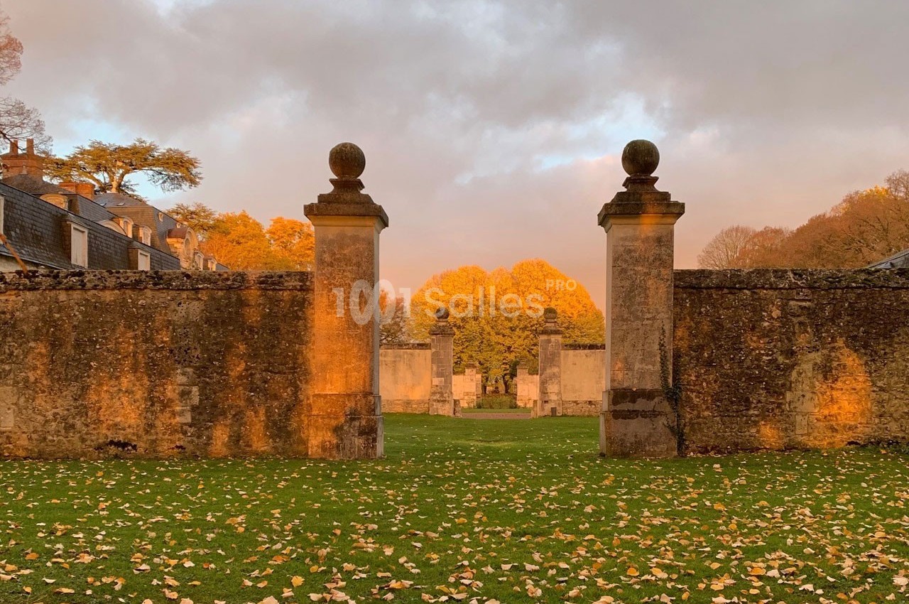 Portail en pierre encadrant une vue sur un parc arboré aux couleurs automnales, éclairé par une lumière dorée.