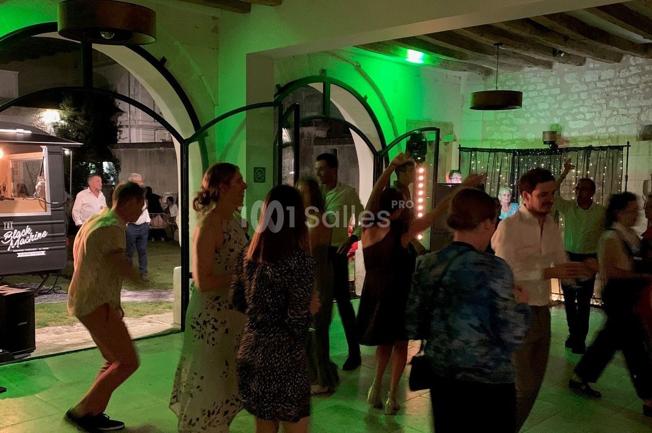 Groupe de personnes dansant dans une salle éclairée de lumières colorées, avec un food truck visible en arrière-plan.
