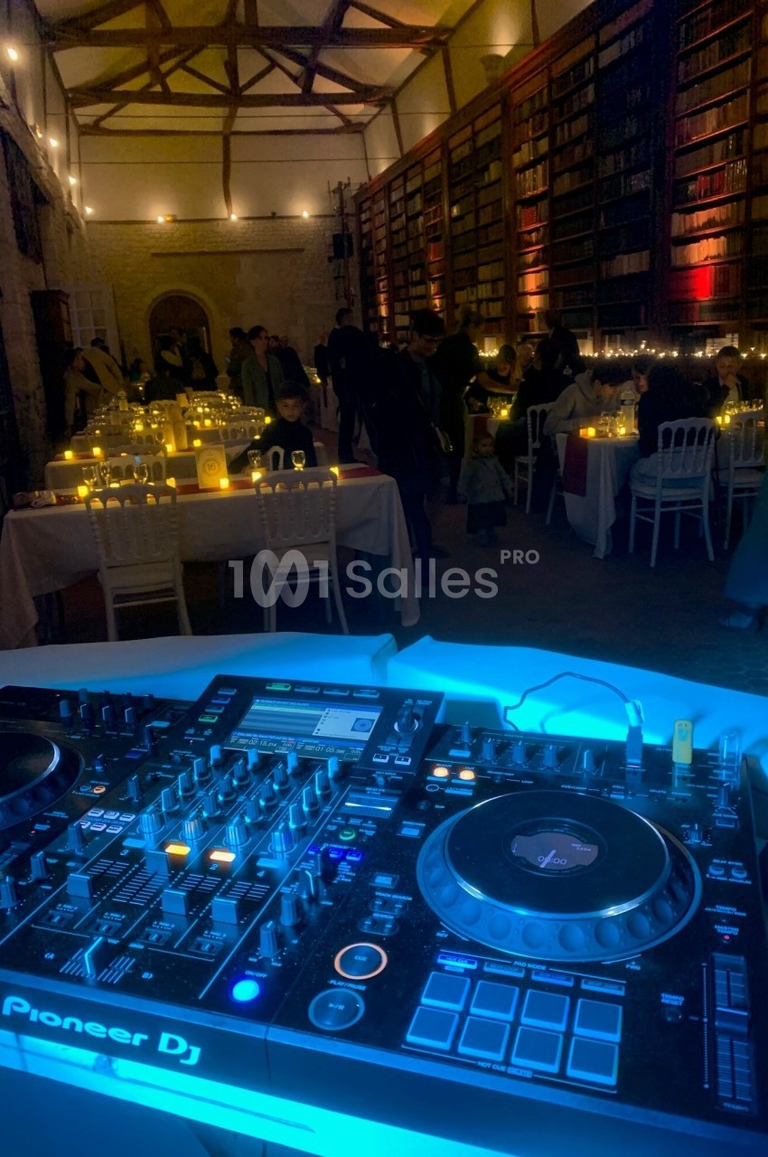 Console DJ éclairée au premier plan, avec une salle de réception décorée et des invités en arrière-plan.