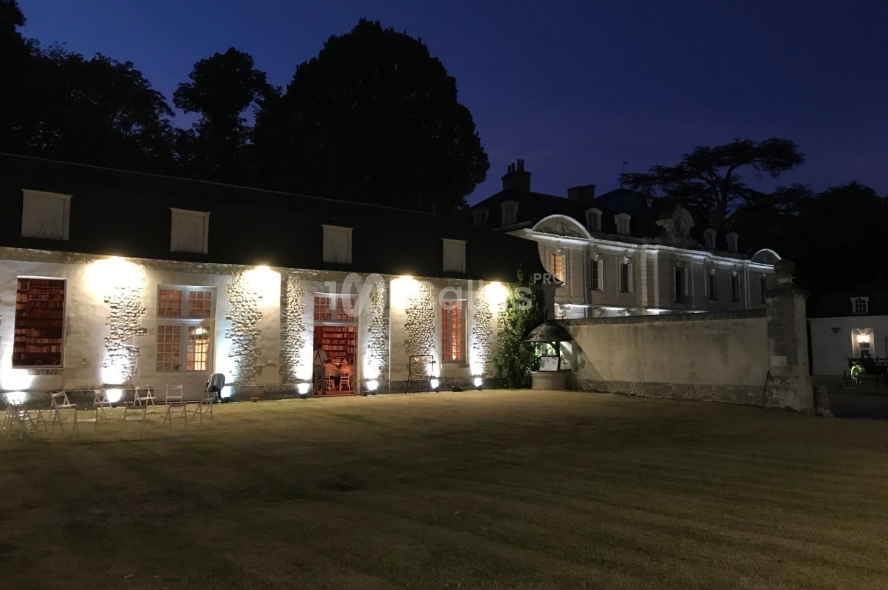 Bâtiment historique éclairé de nuit, avec une pelouse au premier plan et des arbres en arrière-plan.