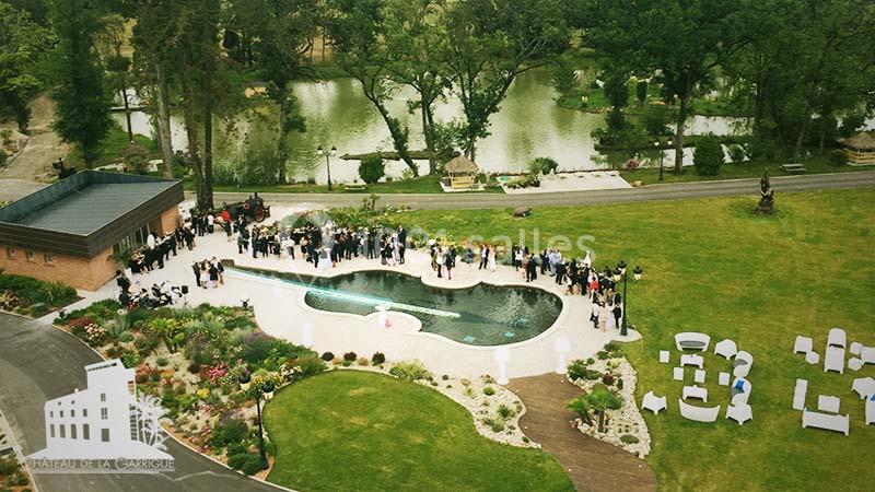 Vue aérienne d'un jardin avec une piscine en forme de haricot, des invités rassemblés et un paysage verdoyant en arrière…
