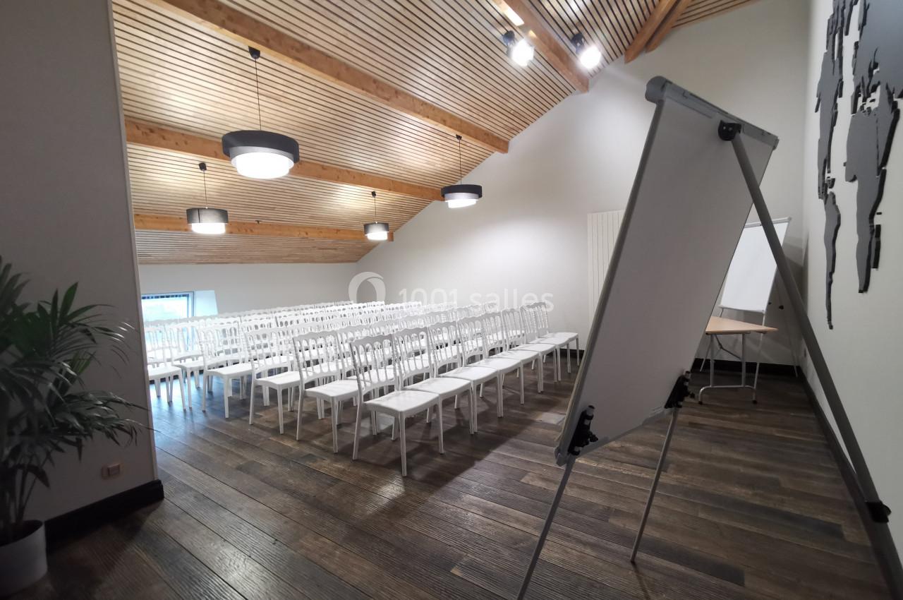 Salle de conférence lumineuse avec des rangées de chaises blanches, un tableau de conférence et un sol en bois sombre.