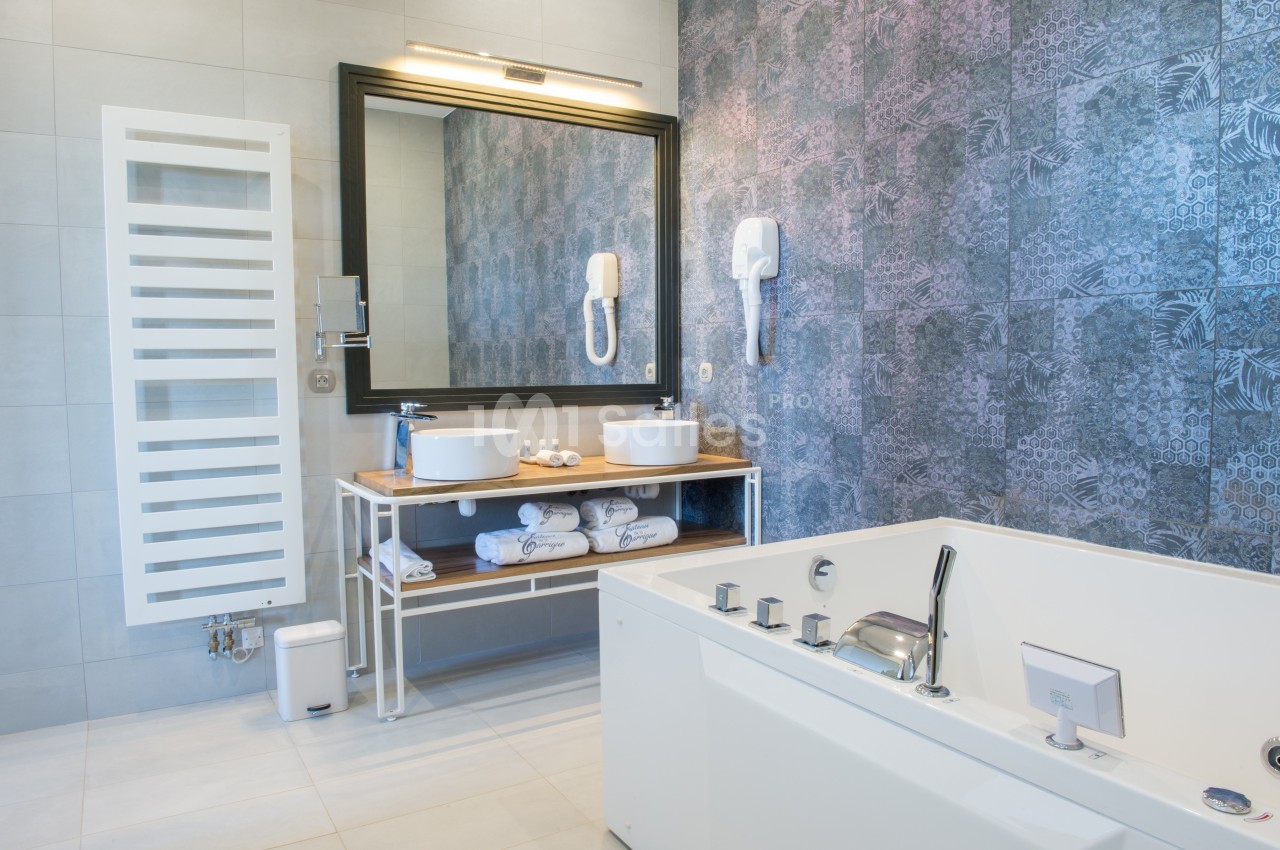 Salle de bain moderne avec baignoire, double vasque sur meuble en bois, miroir encadré et carrelage décoratif.