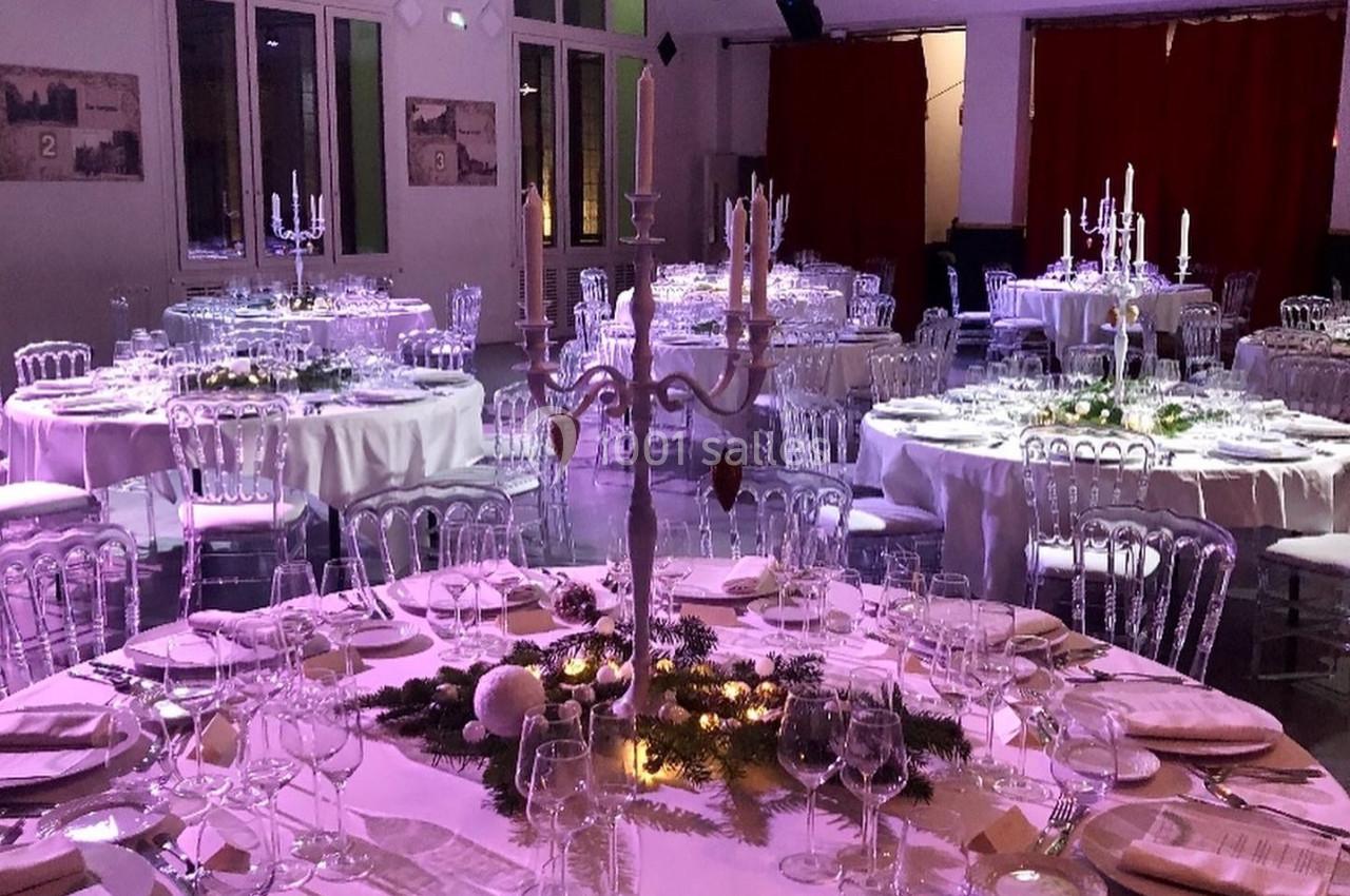 Salle de réception élégamment décorée avec des tables rondes dressées, chandeliers et éclairage tamisé.