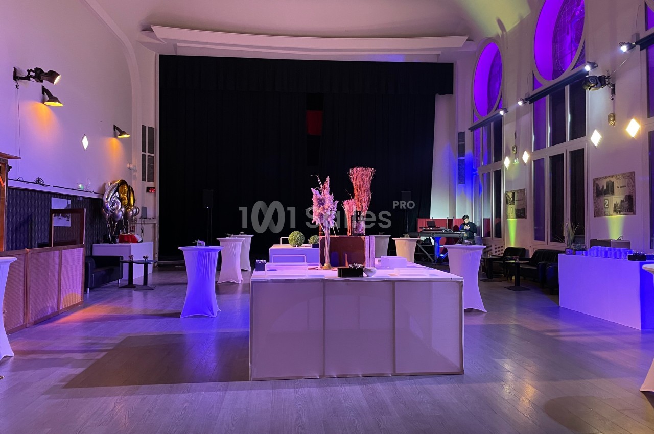 Salle de réception lumineuse avec tables hautes, décor floral et éclairage coloré.
