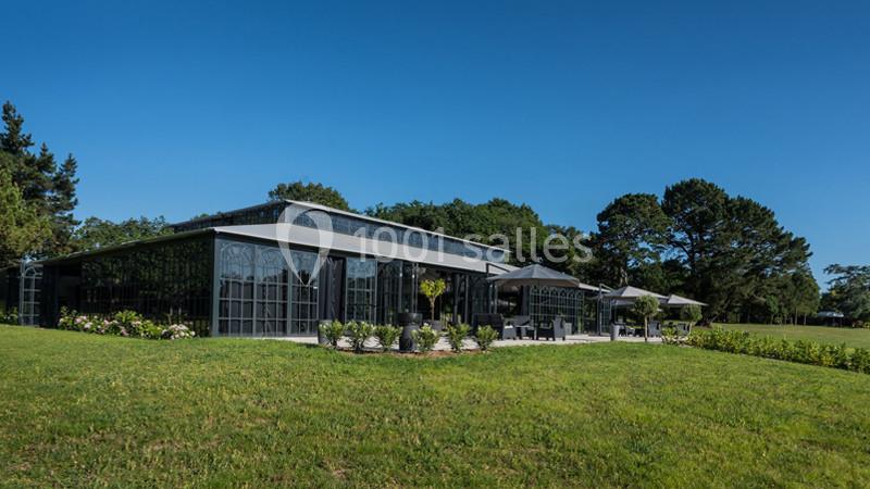 Bâtiment moderne en verre entouré de verdure, avec terrasse aménagée et ciel dégagé en arrière-plan.