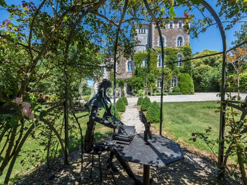 Statue en métal représentant une personne écrivant à une table, située sous une tonnelle devant un bâtiment ancien entouré…