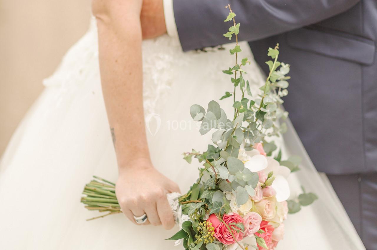 Un couple de mariés en tenue de cérémonie, tenant un bouquet de fleurs pastel avec des touches de vert.