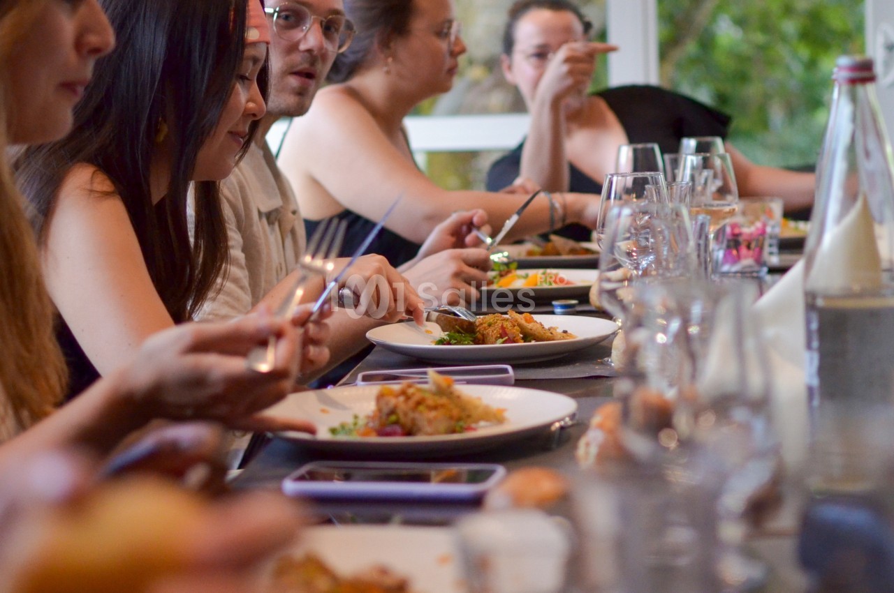 Des convives partagent un repas autour d'une grande table, avec des assiettes et des verres disposés devant eux.