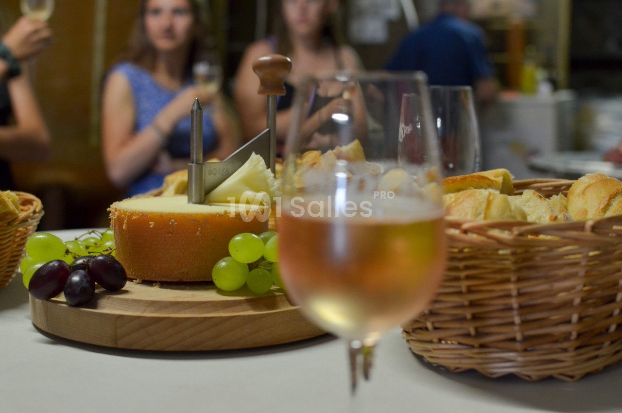 Plateau de fromage avec raisins et pain en arrière-plan, un verre de vin rosé au premier plan.