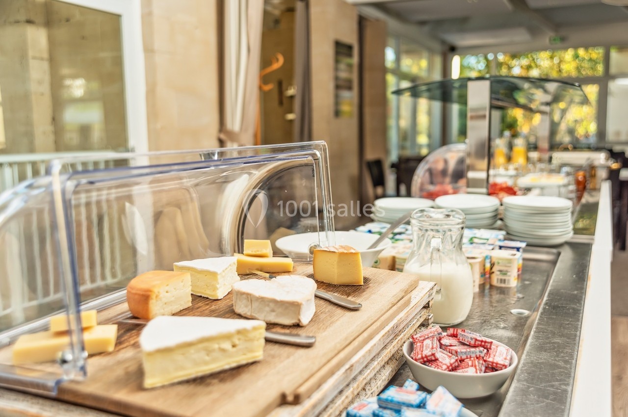 Plateau de fromages variés sur une table de buffet, accompagné de lait, beurre et autres condiments.