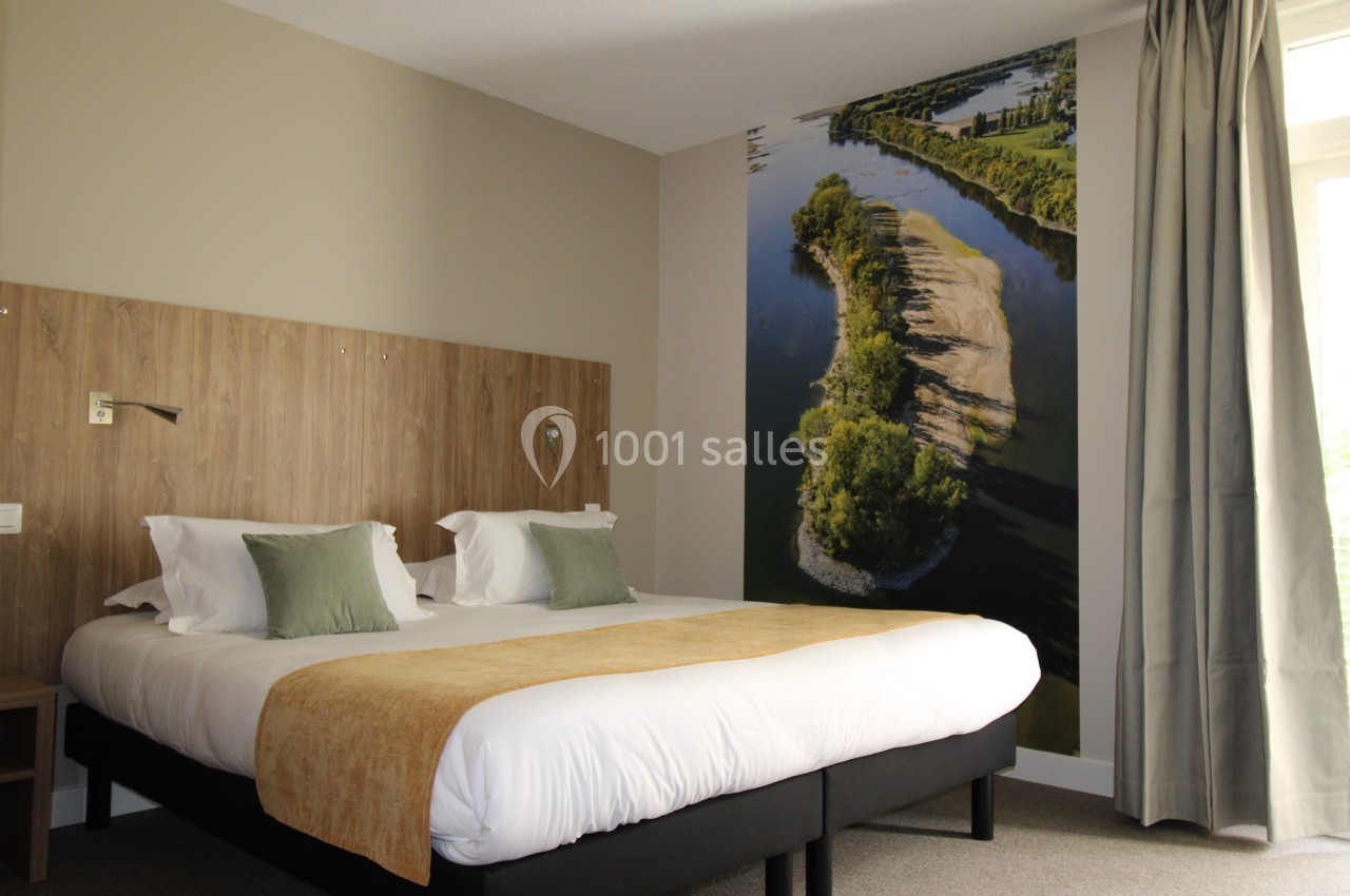 Chambre d'hôtel avec lit double, tête de lit en bois, décor mural représentant une rivière et lumière naturelle.