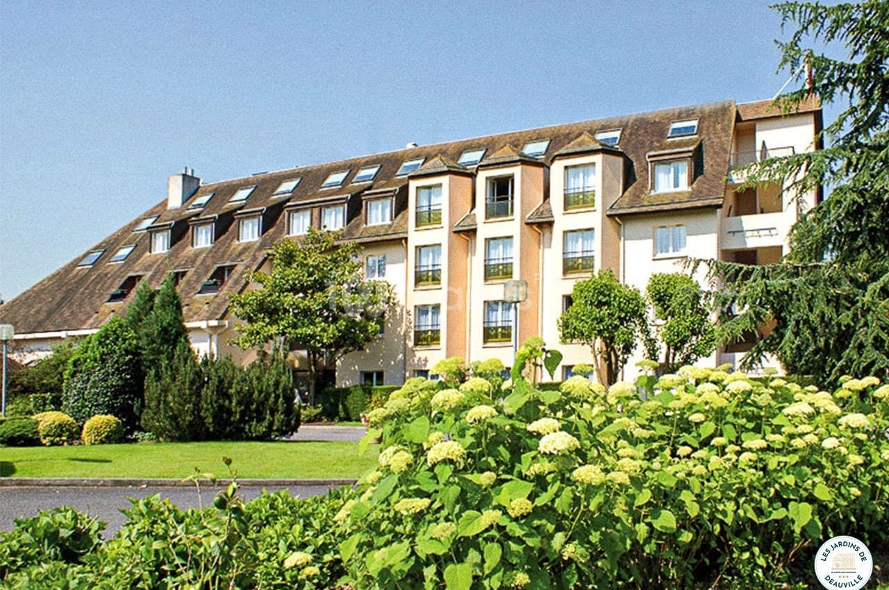 Bâtiment résidentiel entouré de jardins verdoyants avec des arbustes et des fleurs au premier plan.
