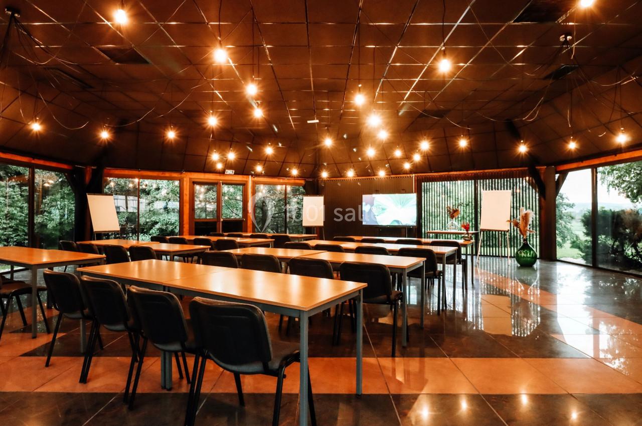 Salle de réunion lumineuse avec des tables, chaises, écrans et grandes baies vitrées donnant sur un espace vert.