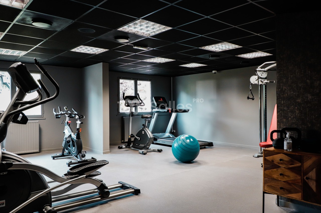 Salle de sport avec vélos d'appartement, tapis de course, ballon d'exercice et équipements de musculation.