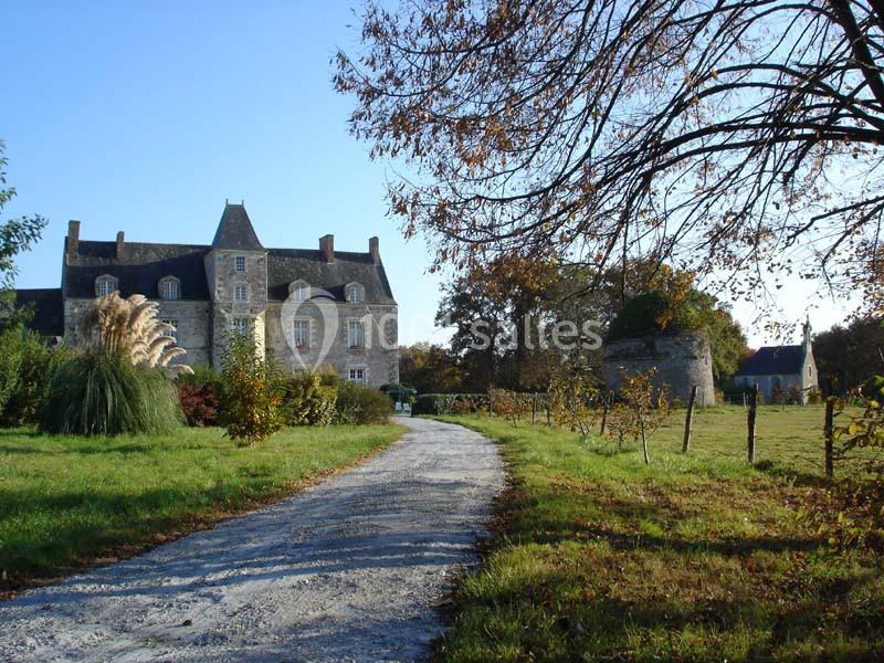 Allée gravillonnée menant à un manoir en pierre entouré de verdure et d'arbres en automne.