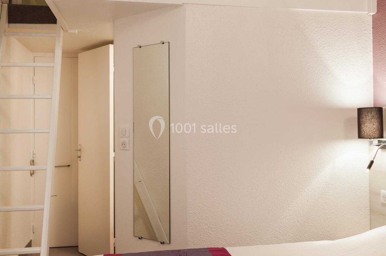 Chambre avec mezzanine, lit double au premier plan, échelle menant à l'étage supérieur, éclairage doux.