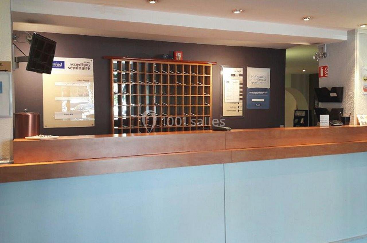 Comptoir d'accueil d'un hôtel avec casiers à clés en bois, panneaux informatifs et éclairage discret.