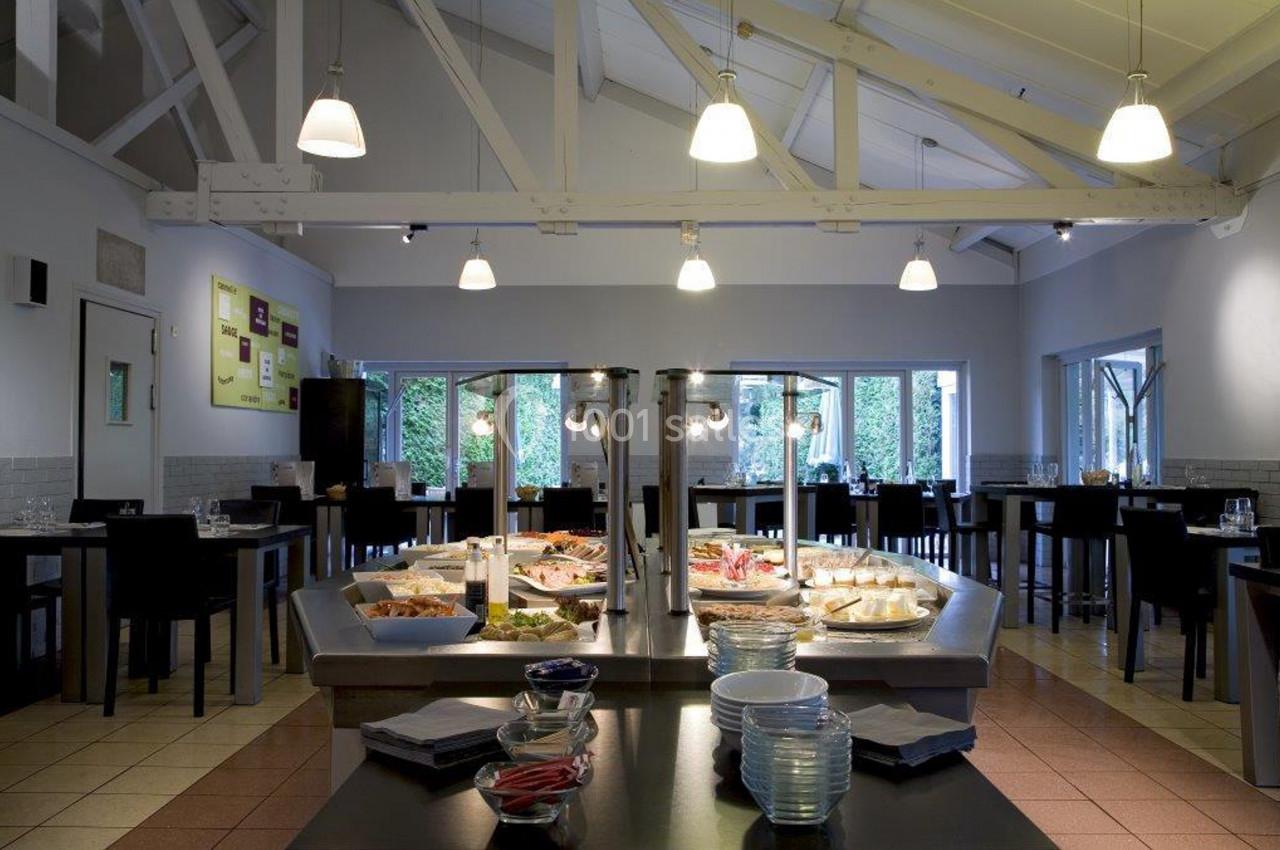 Salle de restaurant lumineuse avec un buffet central proposant divers plats et des tables dressées en arrière-plan.