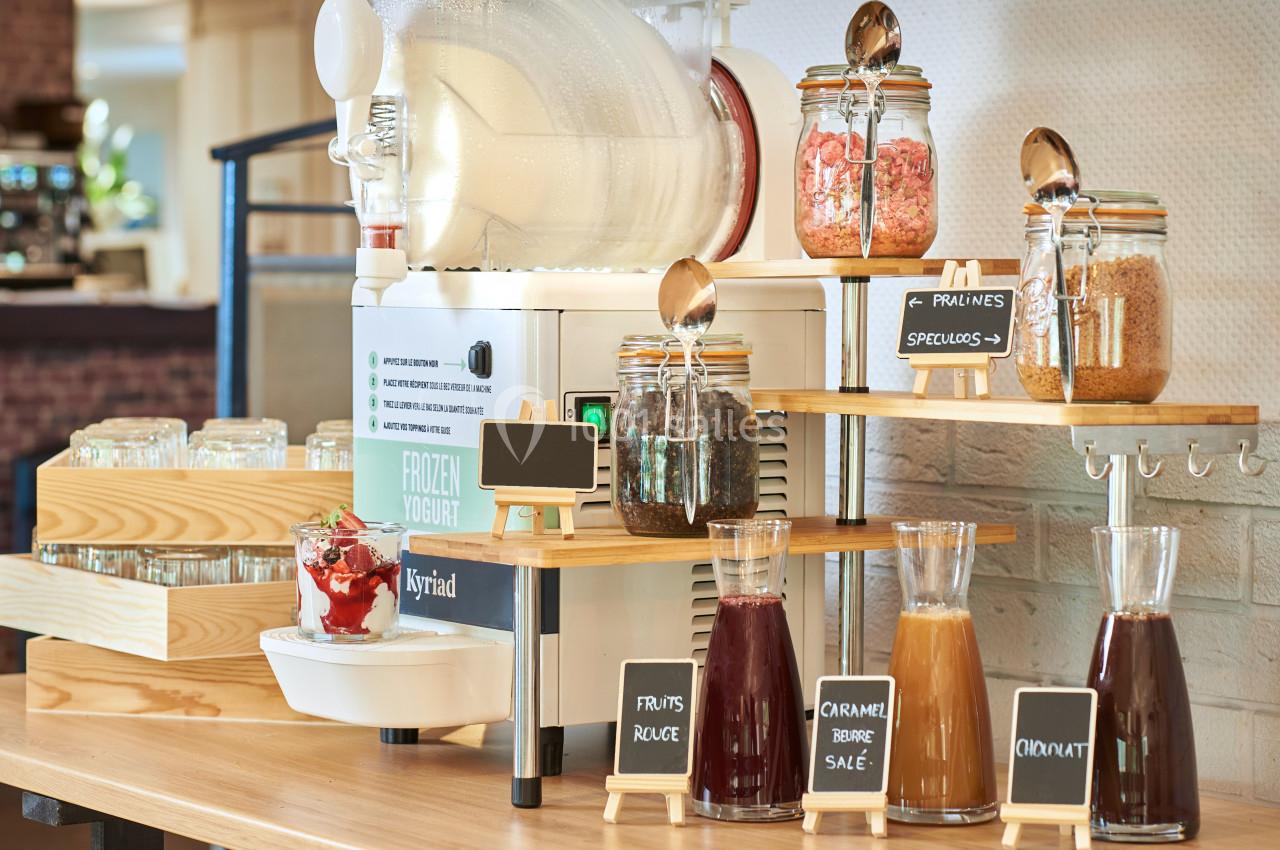 Machine à yaourt glacé avec garnitures variées en pots et carafes, disposées sur un comptoir en bois.