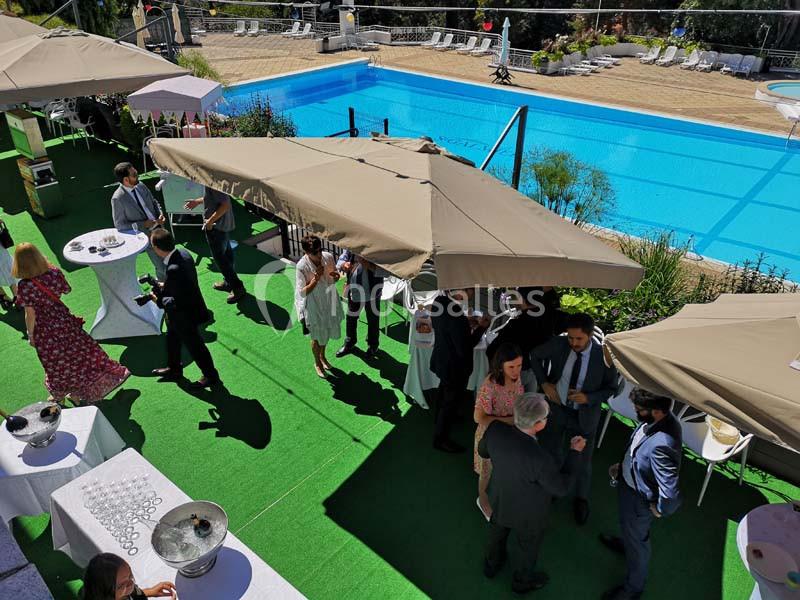 Personnes discutant sous des parasols lors d'un événement en extérieur près d'une piscine.