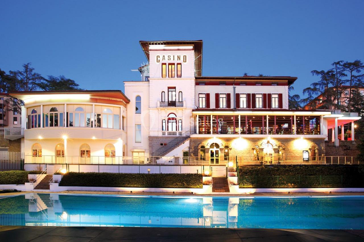 Façade éclairée d'un bâtiment abritant un casino, avec une piscine au premier plan, en soirée.