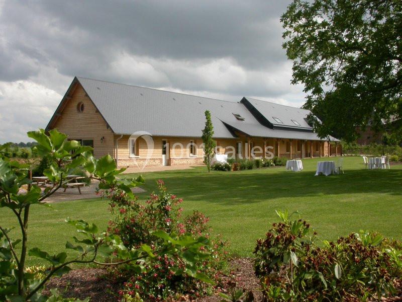 Bâtiment en bois à un étage avec toit gris, entouré de pelouses, arbustes et tables dressées en extérieur.