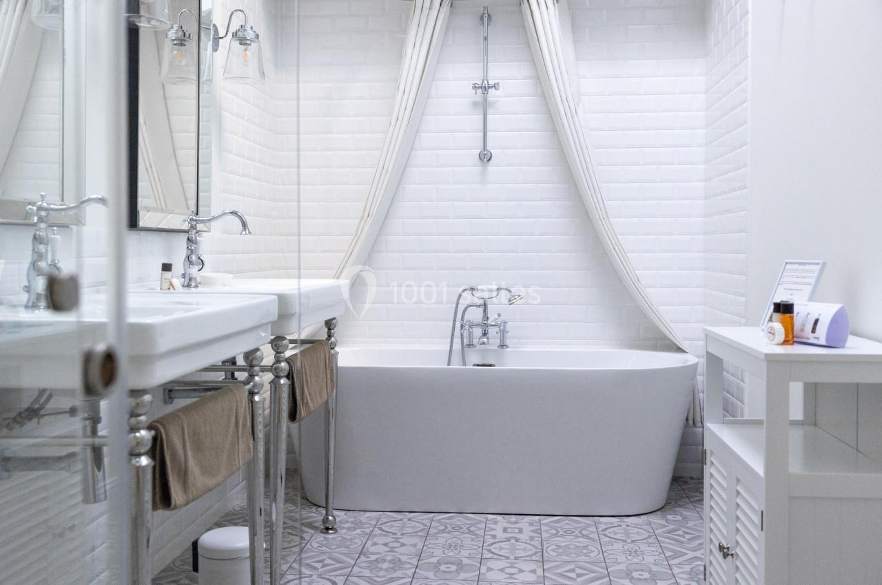 Salle de bain lumineuse avec baignoire blanche, rideaux ouverts, carrelage à motifs et double vasque.
