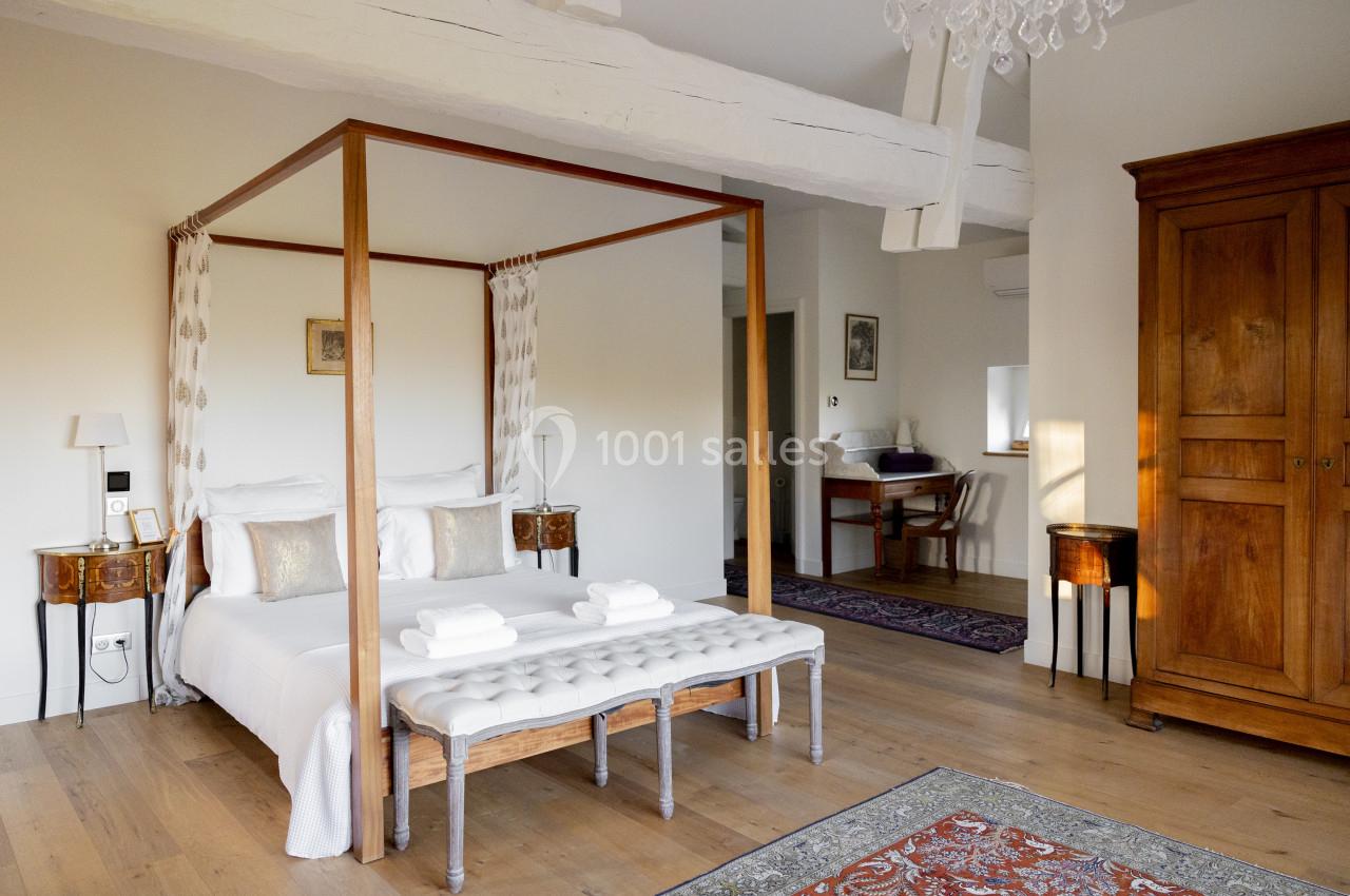 Chambre lumineuse avec lit à baldaquin, meubles en bois, poutres apparentes et décoration élégante.