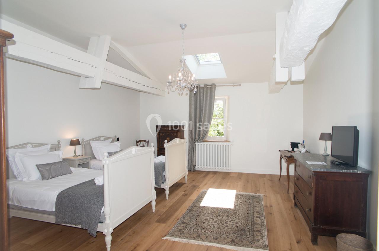 Chambre lumineuse avec deux lits simples, parquet en bois, meubles anciens et plafond avec poutres apparentes.