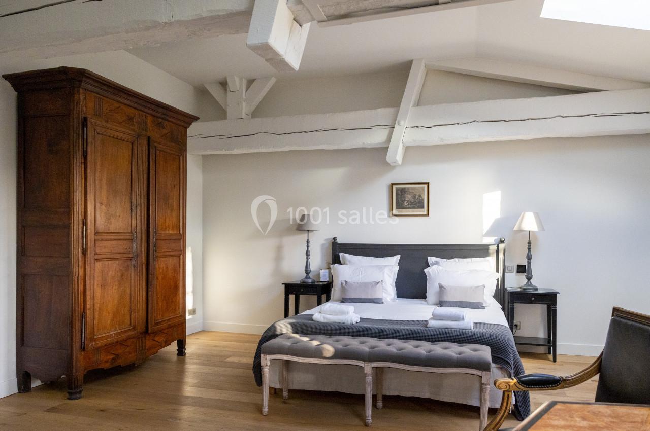 Chambre lumineuse avec lit double, armoire en bois, poutres apparentes et parquet clair.